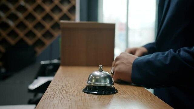 Close-up of male hands ringing call bell in hotel taking key card from receptionist while businessman is arriving and checking-in. Accommodation and people concept.