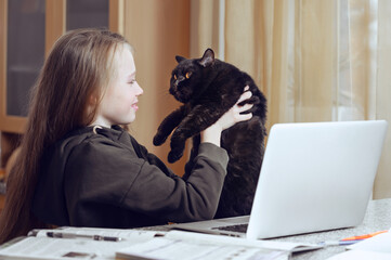 Caucasian teenage girl is learning distant form home using laptop with pet.