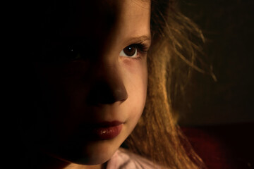 Powerful low key image of little girl in dark side with shadow on face with blissful eyes  looking up dreaming or praying.  Indoor portrait with natural light coming from a window