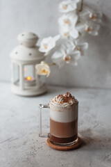 Hot latte macchiato with delicious foam in a tall transparent glass on an easy table setting. Photo in a high key. Breakfast time. Rustic background.