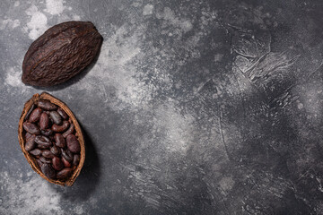 Split fermented cocoa pod with shelled cacao beans atop dark grey backdrop, top view