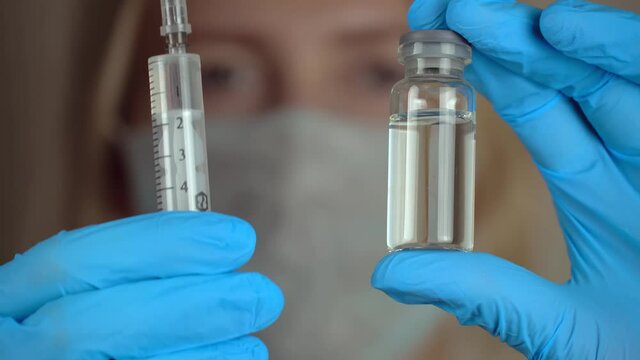 Portrait woman doctor in white hazmat protection holding vaccine ampoule in hand close-up. Coronavirus vaccination. New medication. Health care concept.