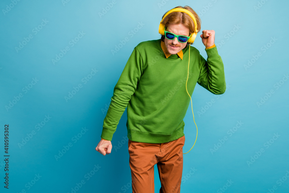 Poster Photo of young handsome funny funky man in headphones and glasses dancing isolated on blue color background