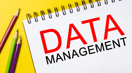 DATA MANAGEMENT on a white notepad with pencils on a yellow background. Business concept