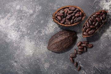 Split fermented cocoa pod with shelled cacao beans atop dark grey backdrop,  top view
