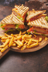 Club sandwiches served on a wooden board. With hot French fries