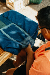Big man sewing running stitch in blue fabric (dyed indigo color). folk art, crafts.