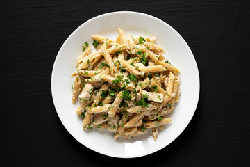 Homemade Chicken Alfredo Penne with Parsley on a black surface, top view. Overhead, from above, flat lay.