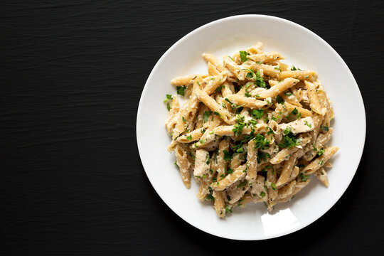 Homemade Chicken Alfredo Penne with Parsley on a black background, top view. Overhead, from above, flat lay. Copy space.
