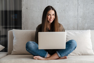 Cheerful brunette nice girl smiling and using laptop on sofa