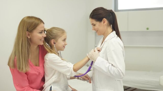 Girl playing with stethoscope in hospital, have fun with doctor woman in medical suit, listen to heartbeat of nurse. Medicine, healthcare concept.