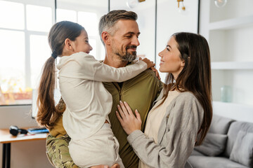 Happy masculine military man smiling and hugging his family indoors - 410597901