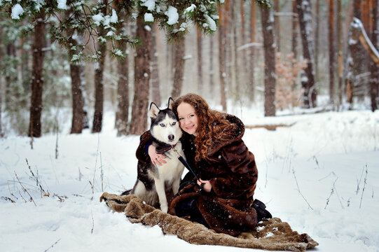 Image of a beautiful girl with a Husky dog in a winter Park. She snuggled up to the dog. A girl in a beautiful fur coat. A man on white snow with a dog. People and dogs.