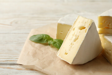 Baking paper with camembert cheese and basil on wooden background
