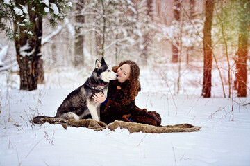 Frame with a beautiful girl and a Husky dog in a winter Park. She looks at the dog tenderly. A man on white snow with a dog. People and dogs. Horizontal orientation.