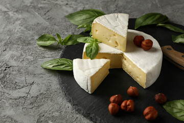 Tray with camembert, hazelnut, basil and knife on gray background