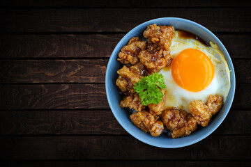 Rice in a bowl with egg and fried chicken with brown butter sauce. Wooden background.