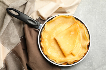 Pan with thin pancakes and kitchen towel on gray background