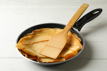 Pan with tasty thin pancakes and spatula on wooden table