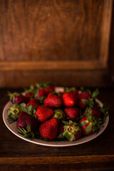 a plate full of fresh strawberries picked from the village garden. photographed in natural light with blurred wooden background