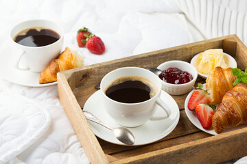 Breakfast in bed, tray with cups of coffee, fresh croissants, jam, strawberries.