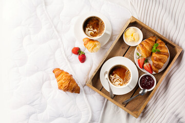 Breakfast in bed, tray with cups of coffee, fresh croissants, jam, fresh strawberries.