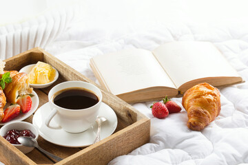 Morning breakfast in bed with cup of coffee, fresh croissants, jam, strawberries.