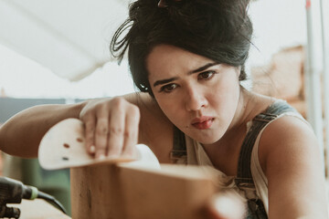 Female carpenter smoothing the lumber with a sanding disc