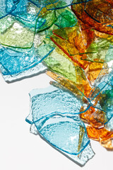 Background of fragments of colored multicolored glass with an iridescent sheen and with blurred reflections on white background. Selective focus
