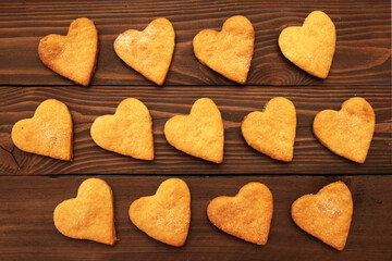Heart cookies for Valentine's Day are laid out on a wooden background.