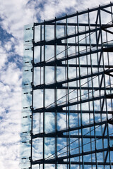 Modern symmetric architecture, glas and steel facade triangle shaped with a blue and cloud sky in the background