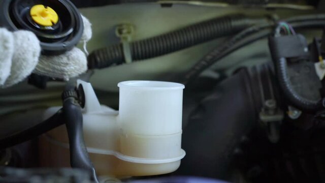 The auto mechanic is refilling additional brake fluid after the inspection and repair of the damaged parts.