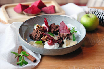 An unusual dessert in a plate of torn sponge cake, beetroot slices, nuts with apple and mint leaves
