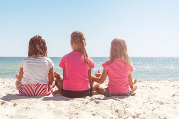 Back view three girls sitting on beach and looking at sea. Close-up Yoga asana, summer fun