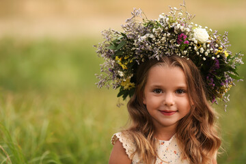 Cute little girl wearing wreath made of beautiful flowers in field