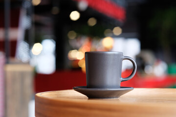 A small black coffee cup on a saucer on a wooden table. Coffee in a cafe on the background of blurred background
