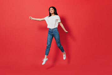 Long-haired woman in stylish outfit jumping on isolated background