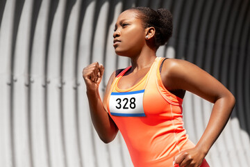 fitness, sport and race concept - young african american woman running marathon with badge number on shirt