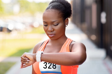 technology, sport and fitness concept - young african american woman or marathon runner with smart...