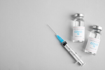 Vials with coronavirus vaccine and syringe on light background, flat lay. Space for text