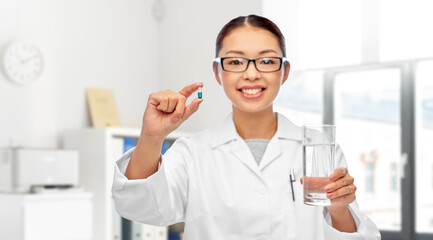 medicine, profession and healthcare concept - happy smiling asian female doctor or nurse pill and glass of water over medical office at hospital on background