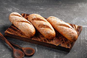 Three loafs of fresh baked baguette on the wooden cutting board on gray background