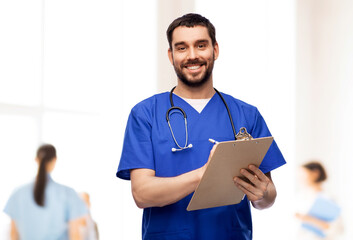healthcare, profession and medicine concept - happy smiling doctor or male nurse in blue uniform...