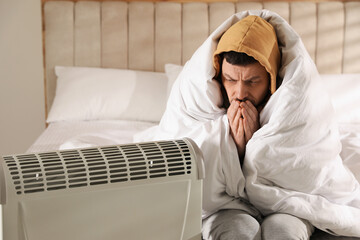 Man sitting in bed near electric heater at home