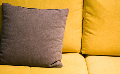 Close up view of a yellow couch with grey pillows in the colours of the year 2021