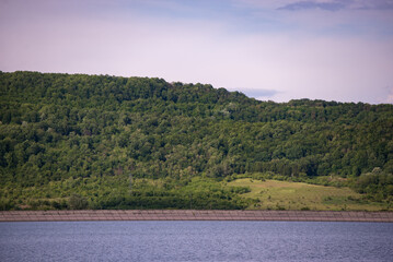 spring landscape with a high hill full of green forest on the edge of a huge lake. a sunny day on the bank of the reservoir
