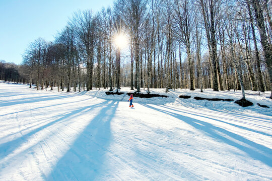 Child walking on snowy ski slope with sunlight on mountain Amiata in Toscana, Italy. Vacation travel concept. Winter activities.