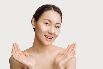 Obraz na płótnie Canvas Beautiful young Asian woman gets cream in her face. The concept of skin care and hydration. a young woman with perfect clean skin health.