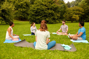 fitness, sport and healthy lifestyle concept - group of happy people sitting on yoga mats at park and talking