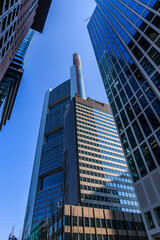 Obraz premium High-rise buildings viewed from below. Blue window facade of commercial buildings in Frankfurt Main. Blue sky in sunny day. Reflections in the glass facade